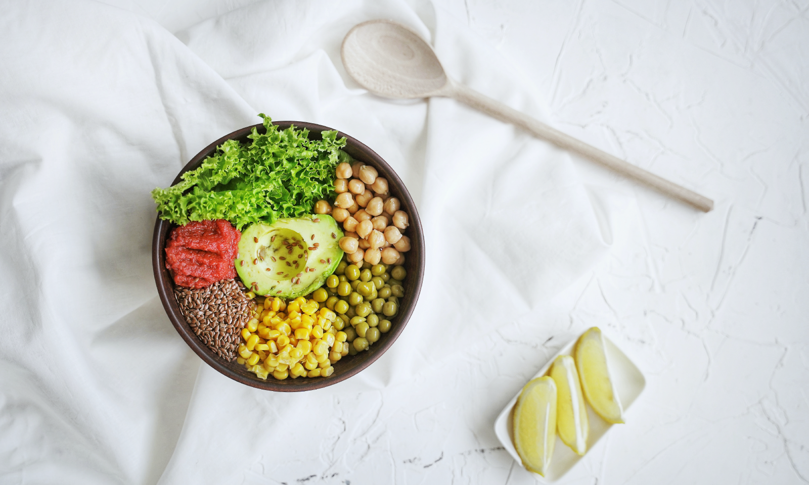 A ceramic bowl filled with healthy food, including grains, legumes, leafy greens and half an avocado.