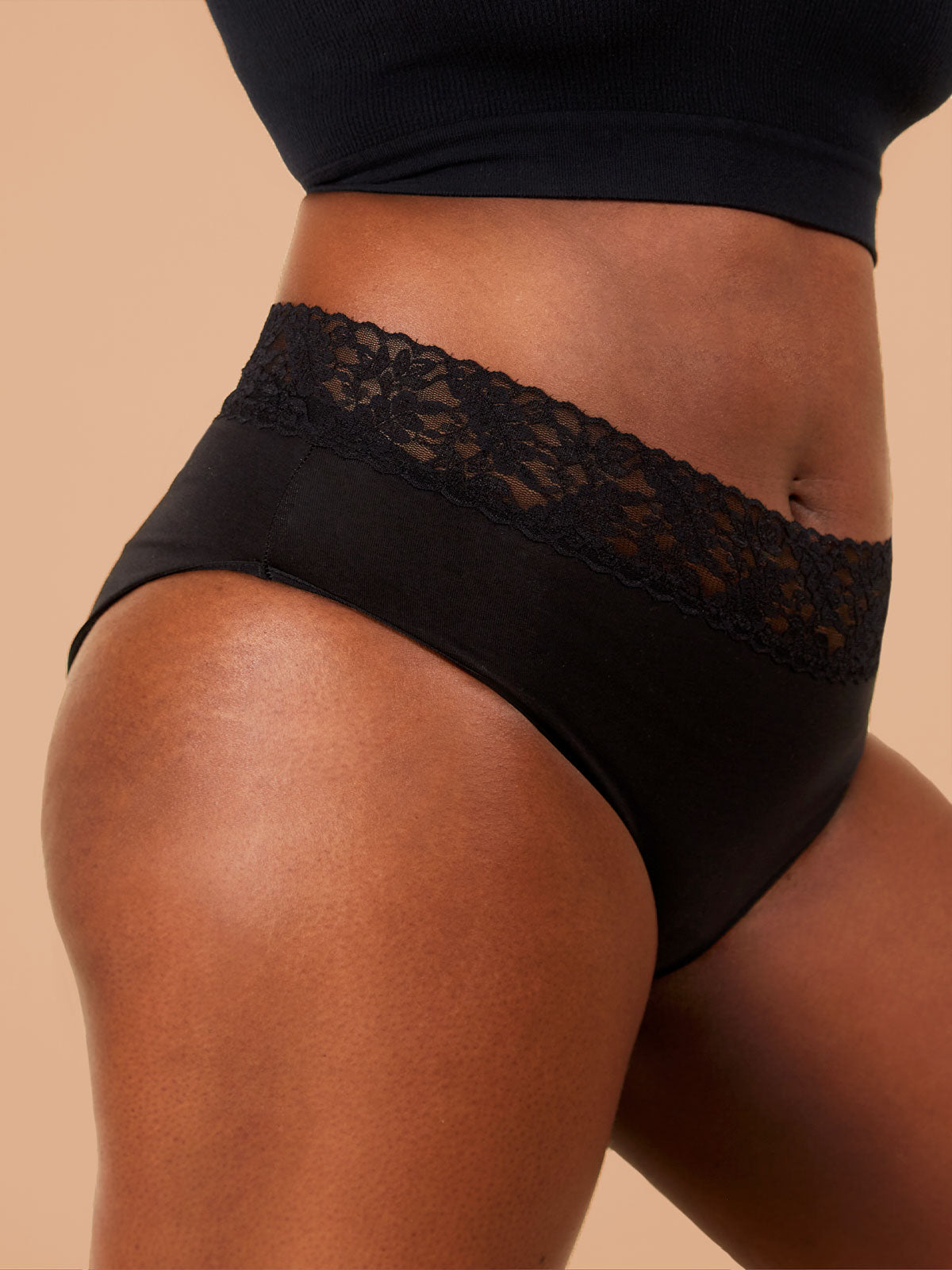 A close-up of a Black woman standing, showcasing black period pants with a floral lace trim. The image highlights the intricate details of the underwear, emphasizing the lace trim and fabric texture.